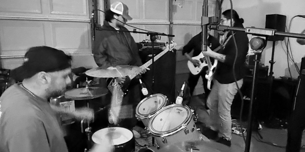 Bassist, drummer, guitarists together. People watching, laptop DAW, cables on floor.